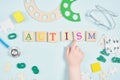 Inscription autism on wooden squares, educational toys and hand of a small child on a blue background Royalty Free Stock Photo