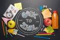 The inscription back to school, on a school board with handles, chalk, an alarm clock, and school breakfast