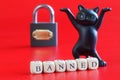 Inscription banned, dancing toy cat and padlock on red background. Concept of firewall, banning internet forum, chat room, website