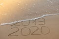 Inscription 2019 and 2020 on beach sand, wave covering 2019 digits. New Year 2020 coming concept