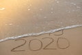 Inscription 2019 and 2020 on beach sand, wave covering 2019 digits. New Year 2020 coming concept