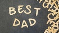 The inscription `best dad` folded of wooden letters on a black table, next to a pile of scattered wooden letters.