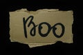 The inscription Boo in black paint on a piece of cardboard on a black background, the concept of the holiday Halloween