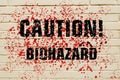 Inscription Caution Biohazard on a bloodstained brick wall.
