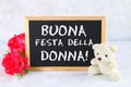The inscription on the chalkboard in Italian: Happy woman`s day. Pink flowers and teddy bear. Royalty Free Stock Photo