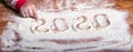 Inscription 2020 with a children`s hand on a flour board New Year background - concept