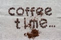 Inscription Coffee Time of a roasted coffee beans on a grey canvas, scattered ground coffee