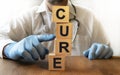 The inscription CURE on wooden cubes. A male doctor in medical gloves pushes cubes. Health and medicine concept