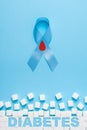 Inscription diabetes blue ribbon awareness with red blood drop and ruined wall made of sugar cubes on a blue background Royalty Free Stock Photo