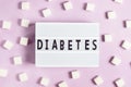 The inscription diabetes on a white board on a pink background with cubes of white sugar