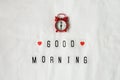 Inscription Good morning, red analog clock, small heart on white rumpled sheets. Top view, flat lay. Horizontal. Concept of rest,