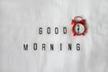 Inscription Good morning, red analog clock on white rumpled sheets. Top view, flat lay. Horizontal. Concept of rest, awakening,