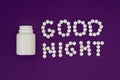Inscription Good night made from white pills. Pill bottle on violet background. Insomnia concept