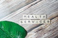 Inscription health services is made of small wooden blocks printed on a wooden background with a green fresh leaf of greenery.