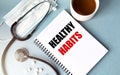 Inscription - HEALTHY HABITS. Written in a notepad to remind you of what`s important. Top view of the table along with a Royalty Free Stock Photo