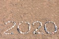 The inscription `2020` laid out by sea pebbles on the sand of the beach. Summer lettering on the coast with copy space for text