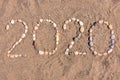 The inscription `2020` laid out by sea pebbles on the sand of the beach. Summer lettering on the coast.