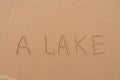 The inscription `Lake` painted on the sand. Royalty Free Stock Photo