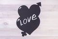 inscription LOVE on black hearts with Cupids arrow. on a light wooden background. Royalty Free Stock Photo