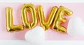 Inscription LOVE foil inflatable golden ballon on the pink background with white hearts. Love, romance and Valentines day concept
