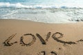Inscription love on the wet sand, a sea wave in the background Royalty Free Stock Photo