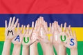 Inscription Maur4itius on the children`s hands against the background of a waving flag of the Mauritius