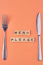 The inscription Menu please on wooden cubes with cutlery on color background. Royalty Free Stock Photo