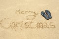 The inscription Merry Christmas on the beach in the sand and beach slippers Royalty Free Stock Photo