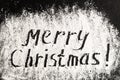 Inscription MERRY CHRISTMAS on powdered sugar background. Royalty Free Stock Photo