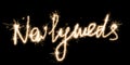 The inscription Newlyweds on a black background with sparklers using a simulated long exposure