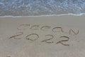 The inscription ocean 2022 on the sand by the water and the rising wave, seashore beach vacation by the sea
