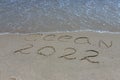 The inscription ocean 2022 on the sand by the water and the rising wave, seashore beach vacation by the sea