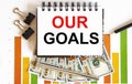 Inscription OUR GOALS in notebook, concept of planning, with office tools ,chart and dollars Royalty Free Stock Photo