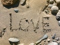 Inscription on river sand `Love` surrounded by colorful stones. Royalty Free Stock Photo
