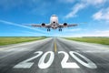 The inscription on the runway 2020 surface of the airport runway with take off aircraft. Concept of travel in the new year,