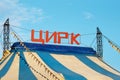 The inscription on the Russian Circus. Striped tent dome against a blue sky with a cloud. Metal supports with stretched