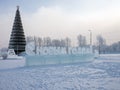 The inscription in Russian - Happy New Year! carved out of ice stands against the backdrop of a Christmas tree.