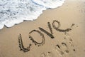 Inscription on the sand love, sea wave, footprints in the sand Royalty Free Stock Photo