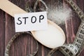 Inscription stop, on a paper sheet, a spoon of sugar and a measuring tape on a wooden background.