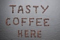 The inscription Tasty coffee here is lined with coffee beans. Rough grey stone background Royalty Free Stock Photo