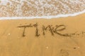 The inscription `time` on the sea sand with the incoming wave. Sandy beach with waves. Royalty Free Stock Photo