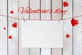 The inscription Valentine`s day is located above the greeting card surrounded by red hearts on a white wooden background with moc