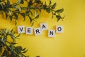 The inscription verano in spanish on the letters of the keyboard on a yellow background with branches of flowers