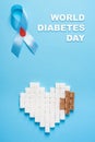 Inscription world diabetes day, blue ribbon awareness with red blood drop, broken heart of sugar cubes, blue background Royalty Free Stock Photo