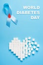 Inscription world diabetes day, blue ribbon awareness with red blood drop, broken heart of sugar cubes, blue background Royalty Free Stock Photo