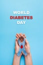 Inscription world diabetes day and blue ribbon awareness with red blood drop in woman hands on a blue background