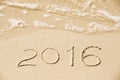 2016 inscription written in the wet yellow beach sand being wash Royalty Free Stock Photo