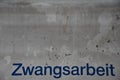 Inscription: `Zwangsarbeit` painted on white wall