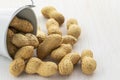 Inshell peanuts spilled out of a bucket on a white wooden background