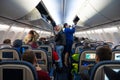 Inside inside the aircraft before departure. Passengers in the aisle stuff their luggage on the upper shelves. Stewardess helps